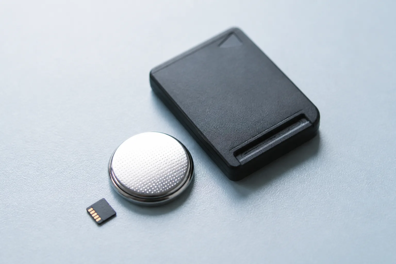 A handheld console in a charging stand next to a notebook, a microSD card in a plastic case and a coffee mug.
